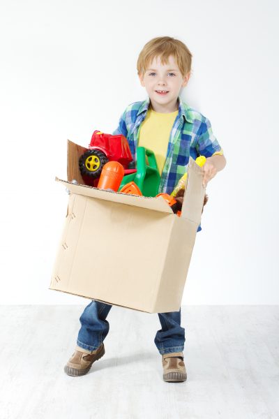 Child holding cardboard box packed with toys. Moving and growing concept